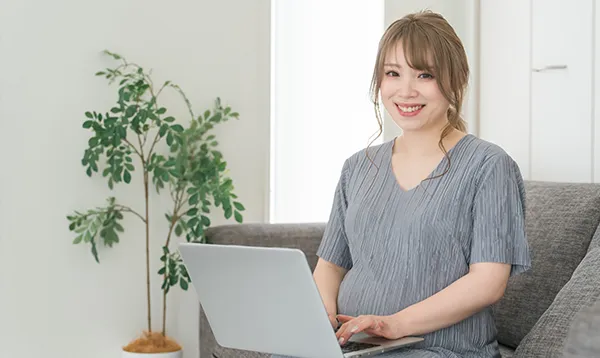 ノートパソコンを使いながら笑顔で座っている女性の写真