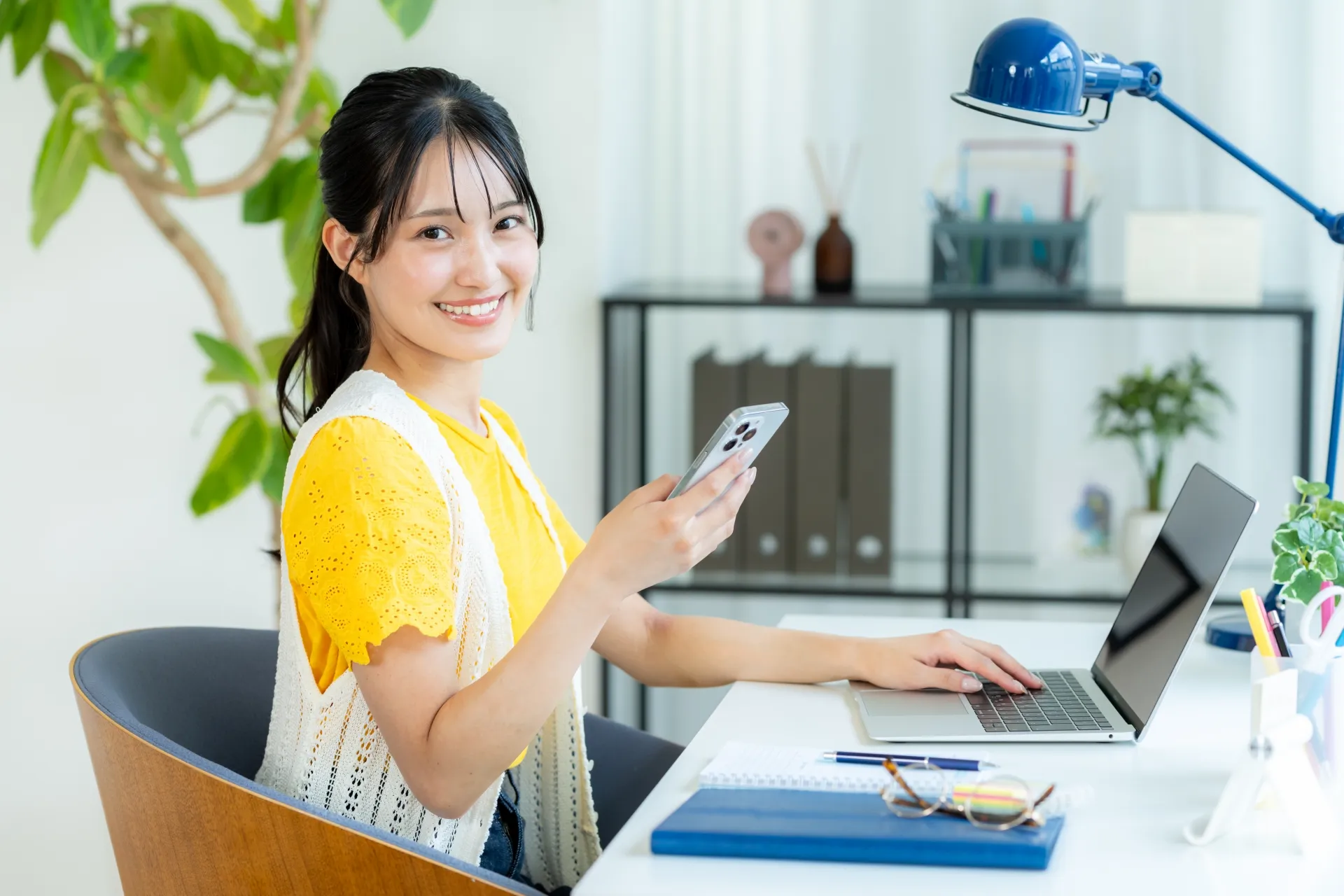 ノートパソコンを使いながら笑顔で座っている女性の写真